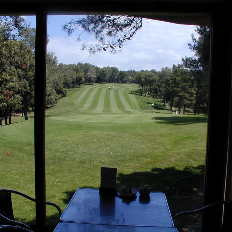 Ein Blick aus einem Fenster auf einen grünen Golfplatz mit gepflegten Rasenflächen und Bäumen