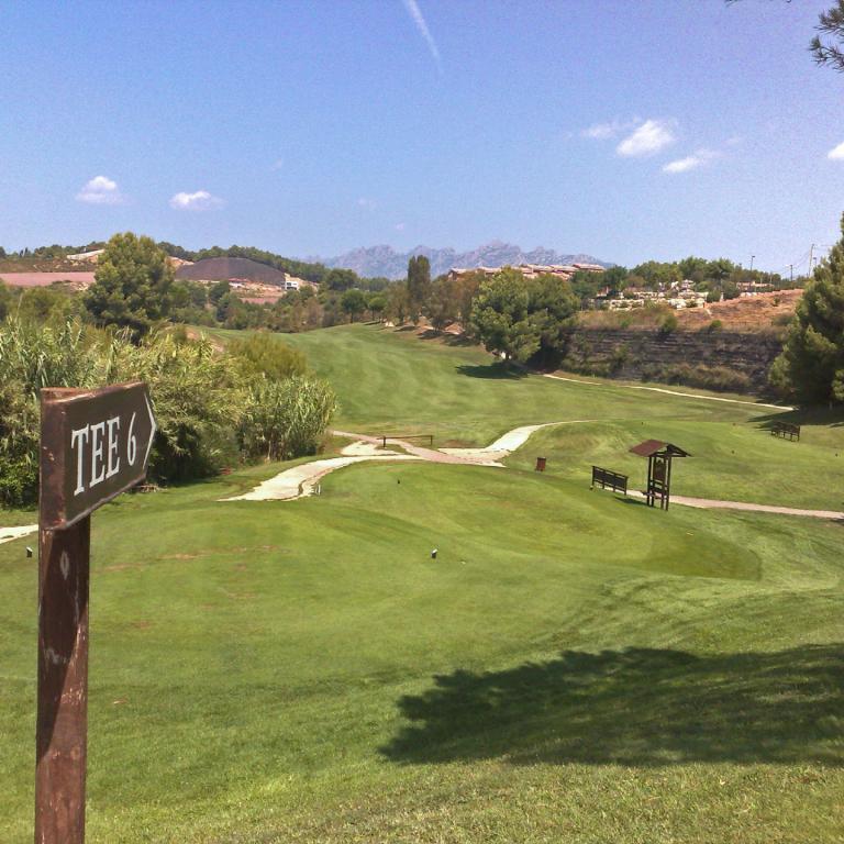 Ein Golfplatztee-Schlagplatz mit der Markierung TEE 6, der einen weiten Blick auf das grüne Gelände und die Hügel im Hintergrund freigibt.