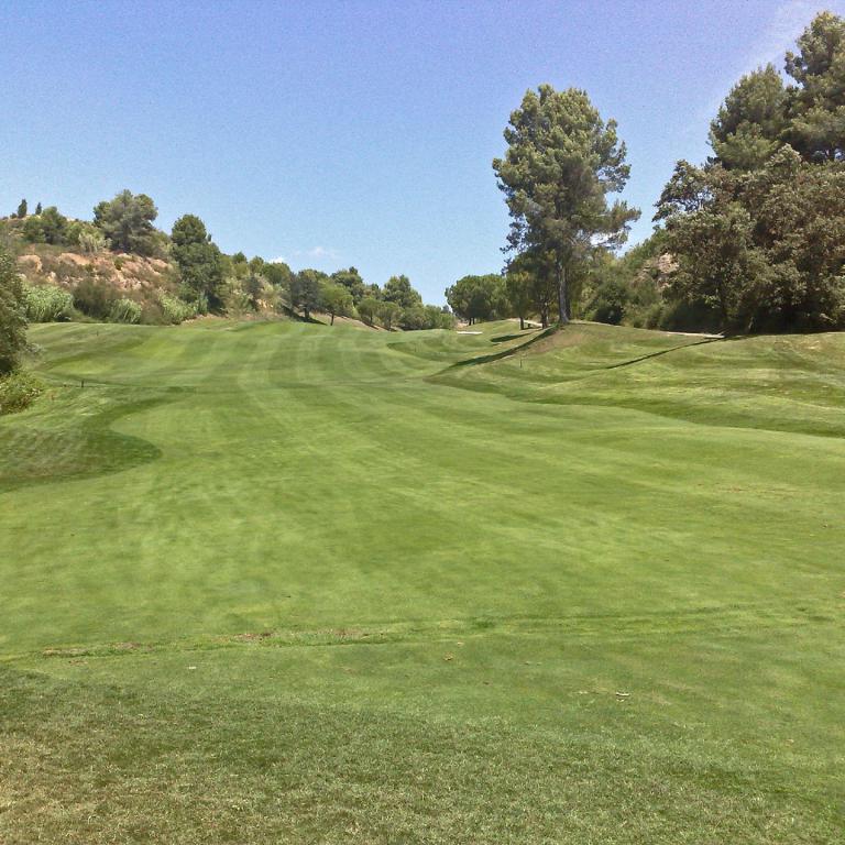 Weitwinkelansicht eines gepflegten Golfplatzes mit grünen Rasenflächen unter blauem Himmel.