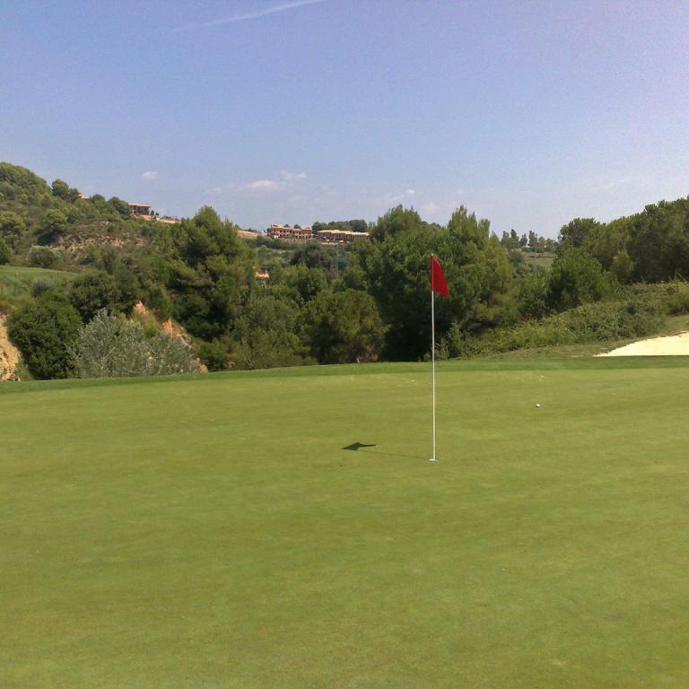 Weitwinkelaufnahme eines Golfplatzes mit einem Fahnenmast und einer Sandbunkerlandschaft im Hintergrund.