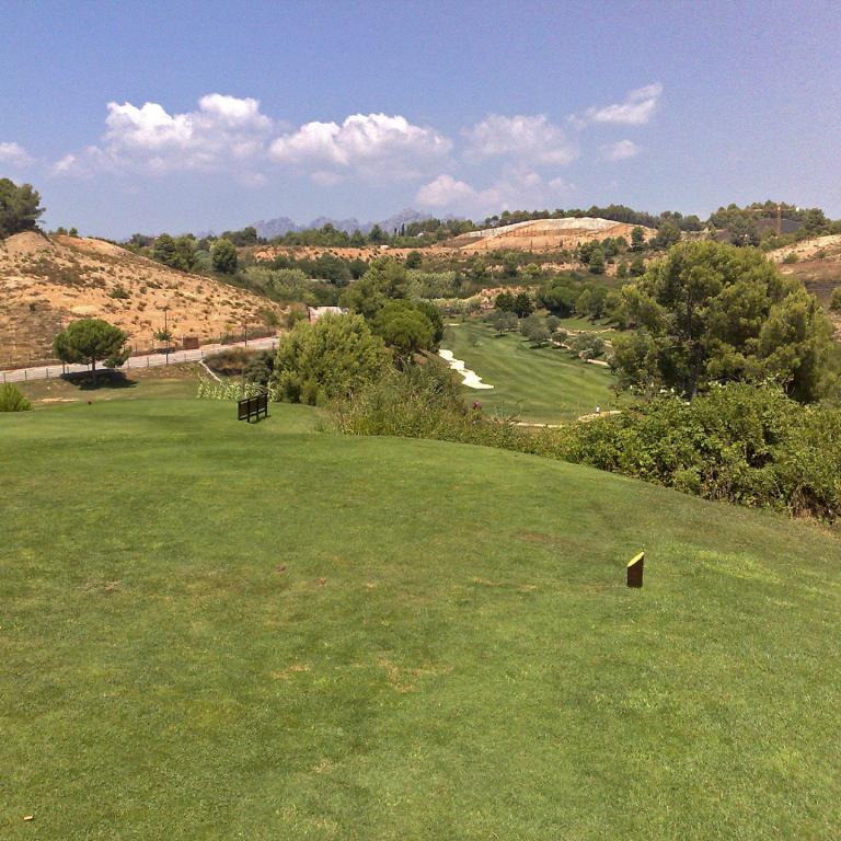 Eine weite grüne Landschaft mit einem Golfplatz, Bäumen und einem blauen Himmel mit Wolken.