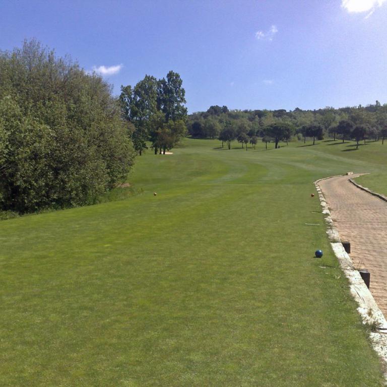 Sonnenaufnahme eines Golfplatzes mit einem gewundenen Pfad, saftig grünem Rasen und Bäumen im Hintergrund.