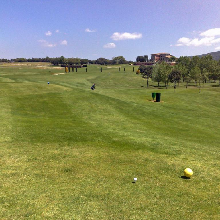 Weitläufiger Golfplatz bei blauem Himmel mit Blick auf die fernen Hügel.