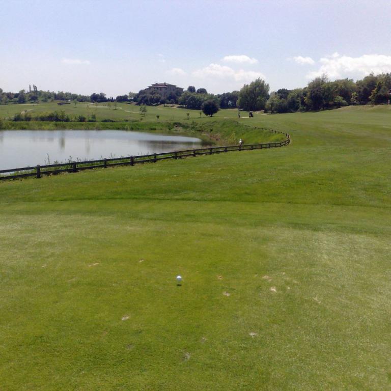 Ein Golfplatz mit einem Teich im Mittelgrund und einem gepflegten Rasen im Vordergrund unter blauem Himmel.