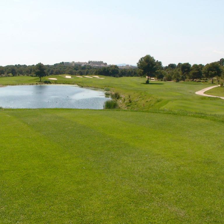 Panoramaaufnahme eines Golfplatzes mit einem großen Teich im Mittelgrund und einer weitläufigen Rasenfläche im Vordergrund.