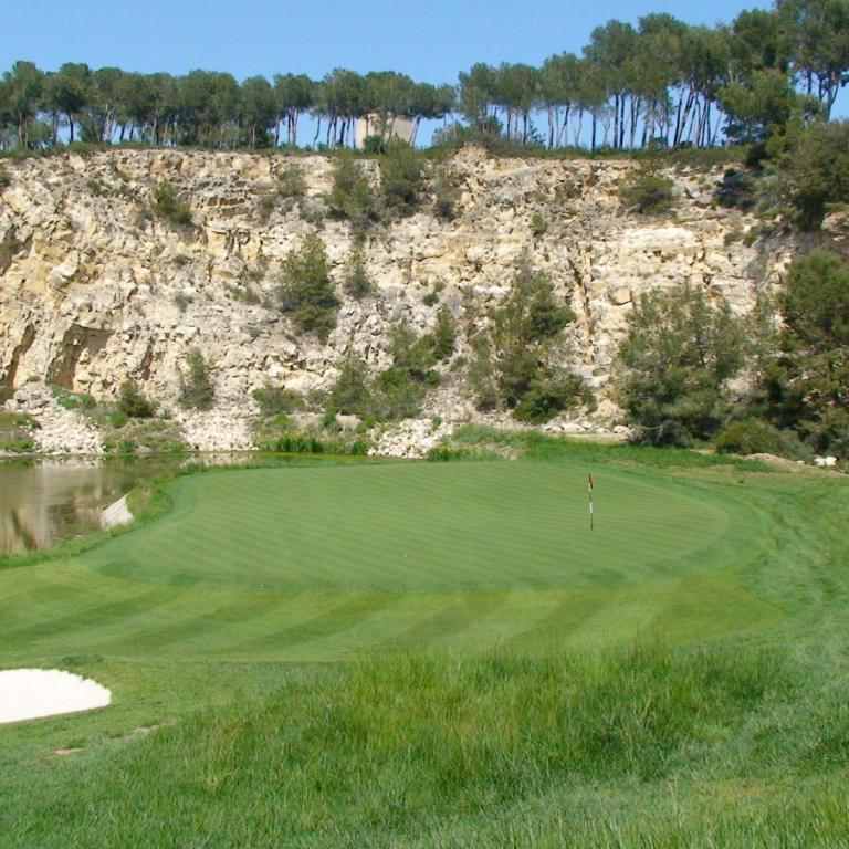 Ein Golfplatz mit Blick auf eine große Felswand, die von Bäumen und einem Gewässer begrenzt wird.