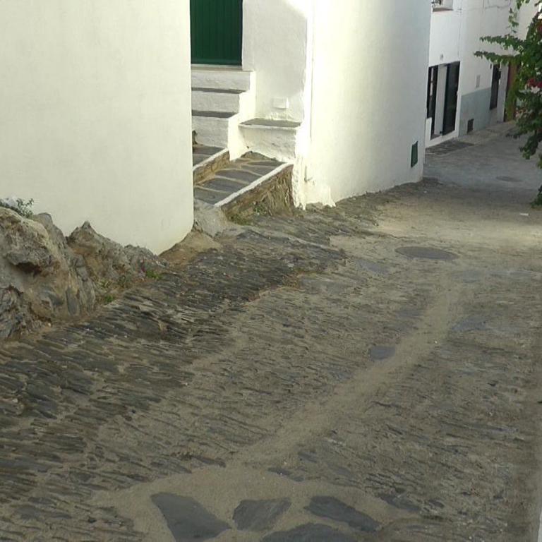 Ein schmaler Durchgang, der von hohen, weißen Mauern begrenzt wird und mit alten Pflastersteinen ausgelegt ist.