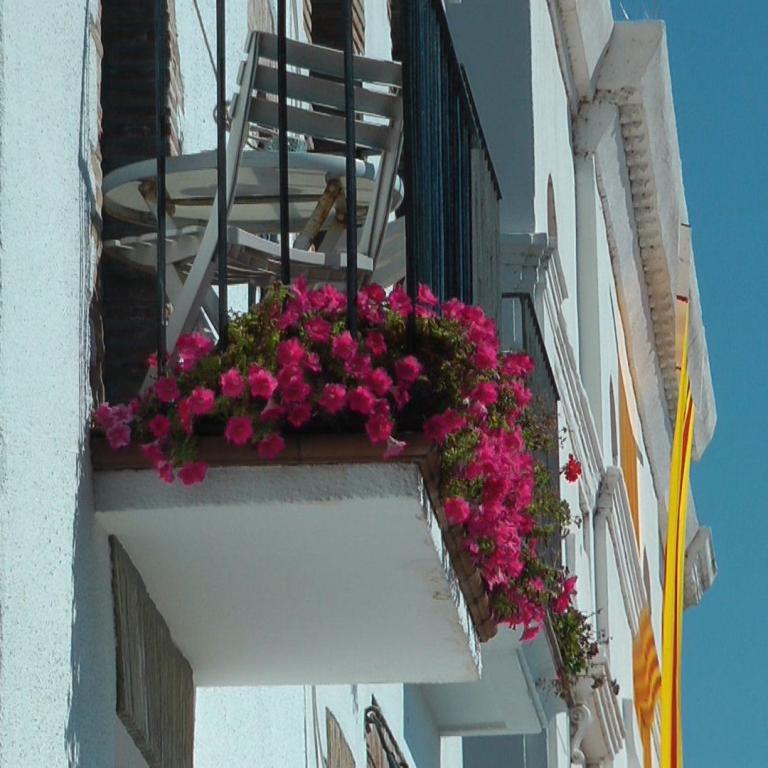 Die Fassade eines Gebäudes mit Balkonen, die mit leuchtend rosa und magenta Blumen dekoriert sind, vor einem klaren blauen Himmel.