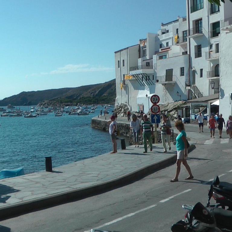 Ein Blick auf eine mediterrane Hafenstadt mit weiß getünchten Gebäuden, einer breiten Promenade und zahlreichen Booten auf dem blauen Meer.