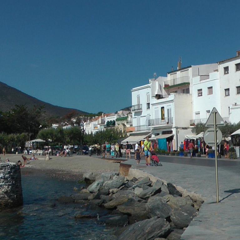 Eine Küstenpromenade mit weißen Häusern, einem breiten Strand und Blick auf die Berge und das Meer.