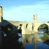 Eine historische Steinbogenbrücke überspannt einen Fluss und ist an ein altes Steingebäude angrenzt.