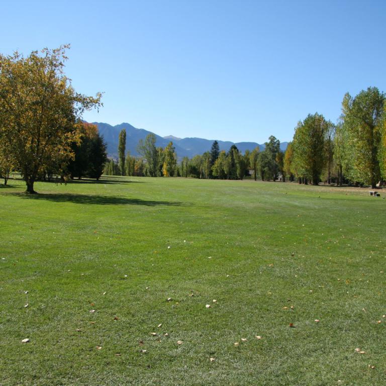 Großes Rasenfeld in einem Park mit Bäumen im Herbstlaub und Blick auf Berge