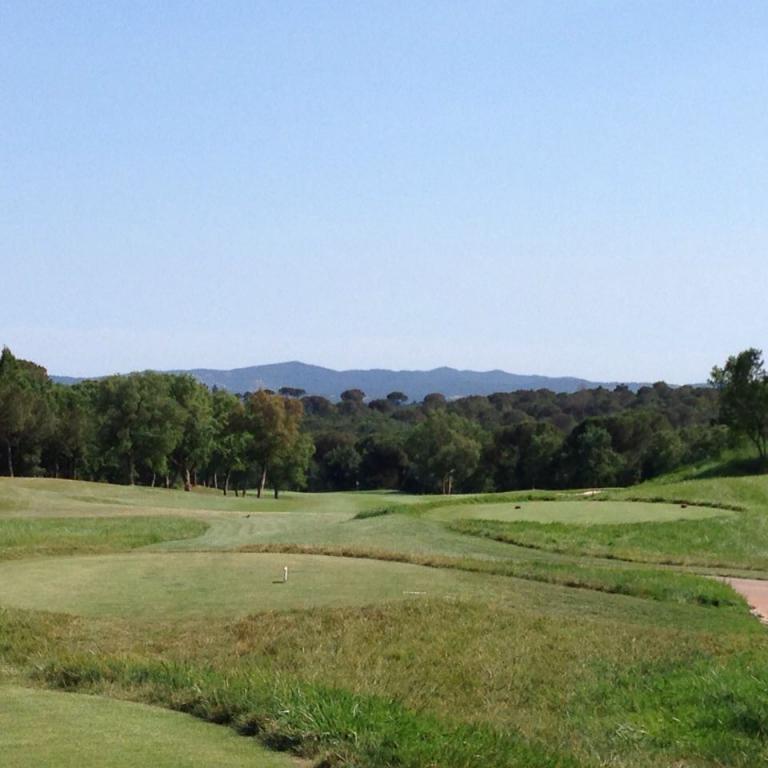 Weitläufiger Panoramablick auf einen Golfplatz mit Blick auf einen Wald und entfernte Bergketten.