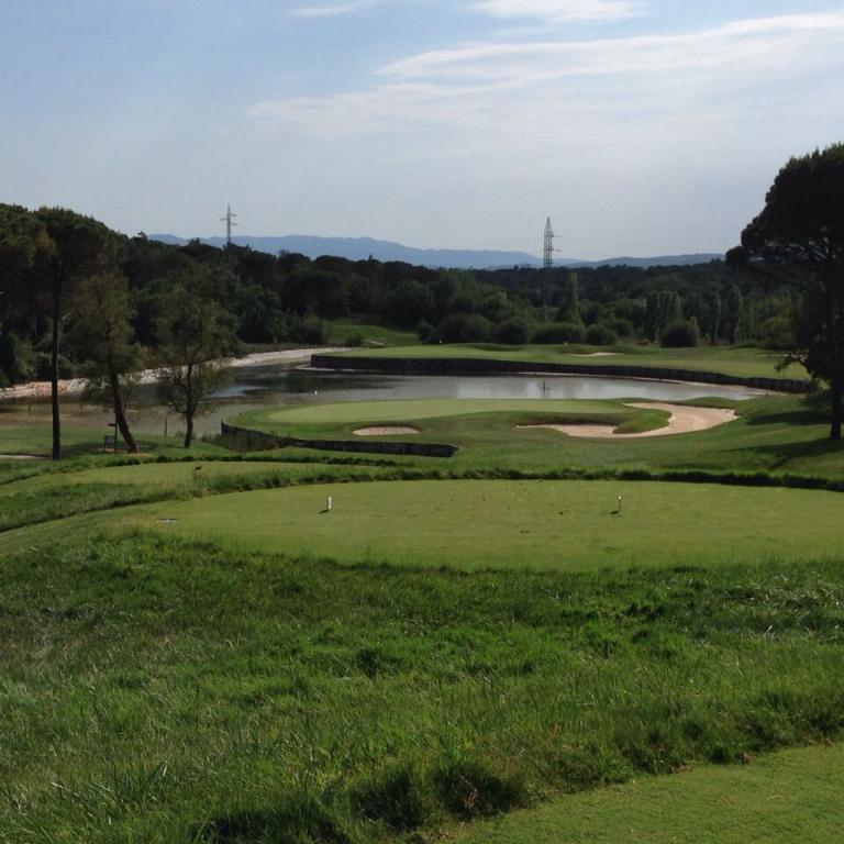Golfplatzlandschaft mit Wasserbecken und umgebenden Bäumen unter blauem Himmel