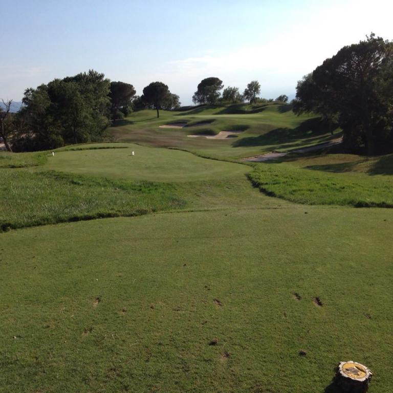 Ein weitläufiges Golfplatzgelände mit grünen Hängen, Bäumen und einem blauen Himmel.