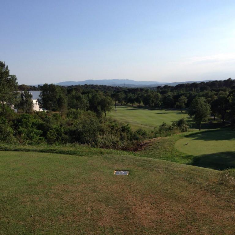 Panoramaausblick auf einen Golfplatz mit Bäumen im Mittelgrund und Bergen unter blauem Himmel