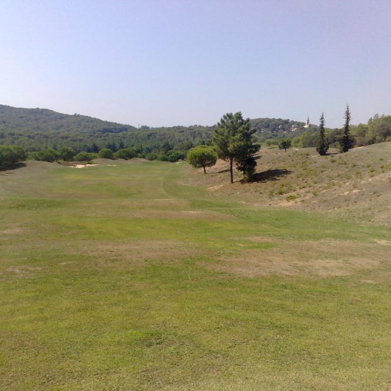 Ein weitläufiger Rasenbereich auf einem Golfplatz mit einem Hang und bewaldeten Hügeln im Hintergrund.