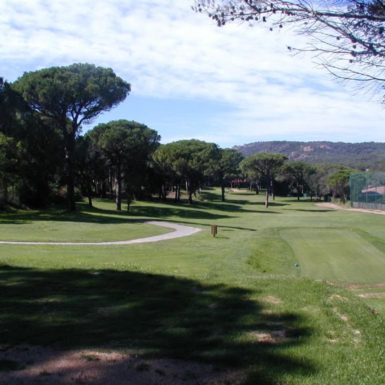 Ein weitläufiger Golfplatz mit grünen Wiesen, Bäumen und einem Blick auf bewaldete Hügel unter einem hellen Himmel.