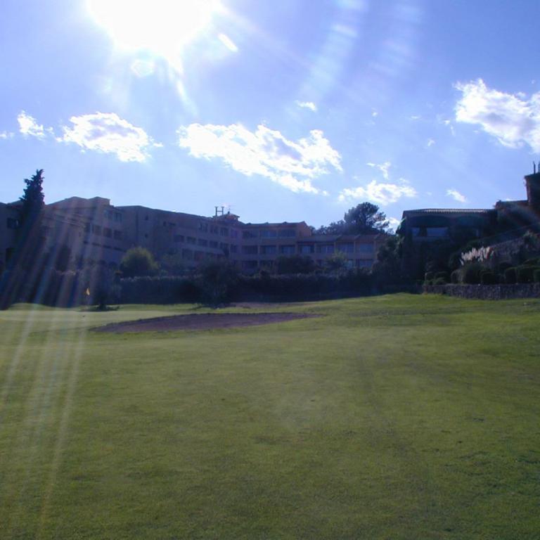 Ein großer, gepflegter Rasen vor einem Gebäudekomplex unter einem hellen, sonnigen Himmel.