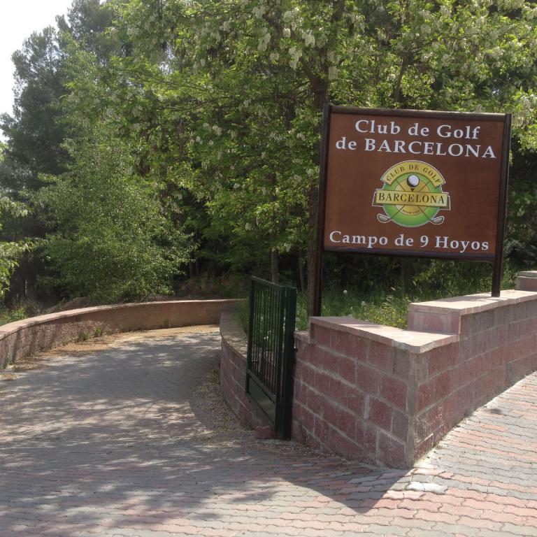 Eingangsschild des Club de Golf de Barcelona mit einem gepflasterten Weg, der in einen bewaldeten Bereich führt.