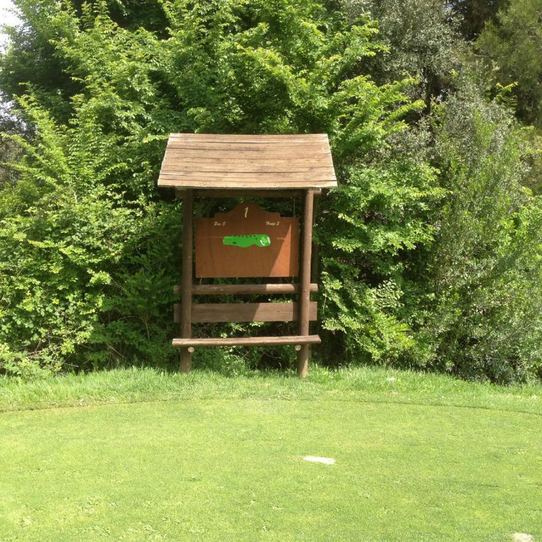 Eine kleine Holzstation steht auf einer grünen Rasenfläche vor einem Hintergrund aus dichtem Laubwerk.