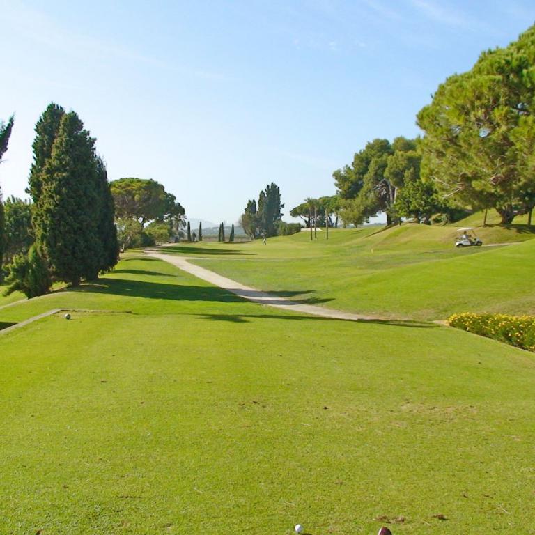 Panoramaaussicht auf einen gut gepflegten Golfplatz mit weiten Rasenflächen und Bäumen.