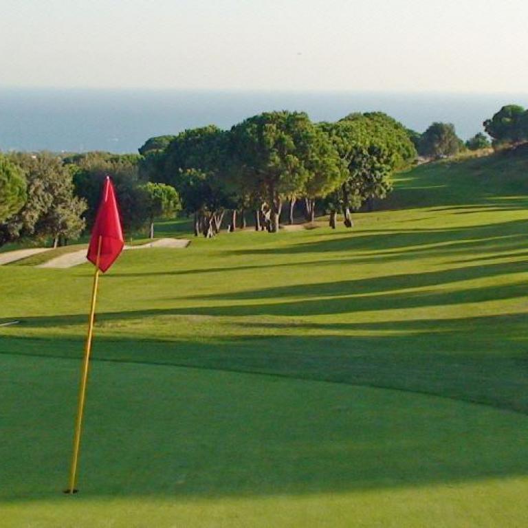 Ein weitläufiger Golfplatz mit Blick aufs Meer, auf dem ein Fahnenpfahl mit roter Flagge steht.