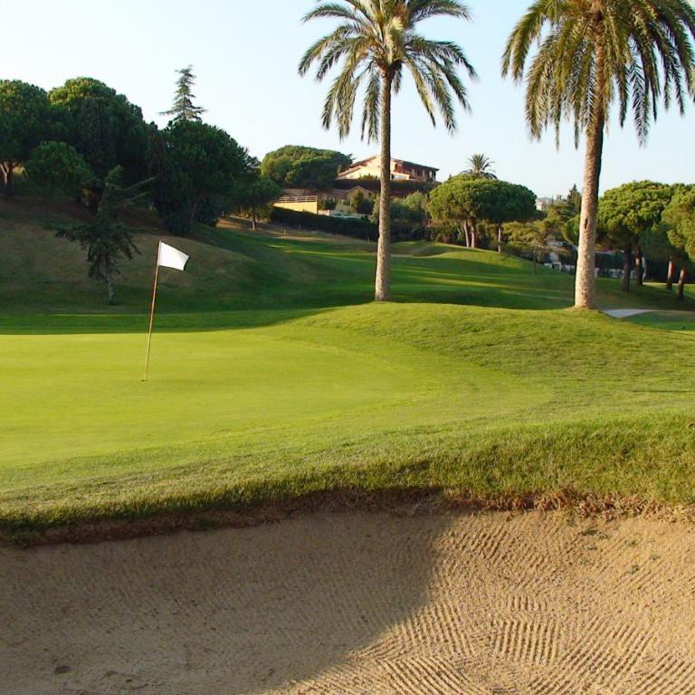 Panoramablick auf einen Golfplatz mit Sandbunker und grüner Wiese im Vordergrund.