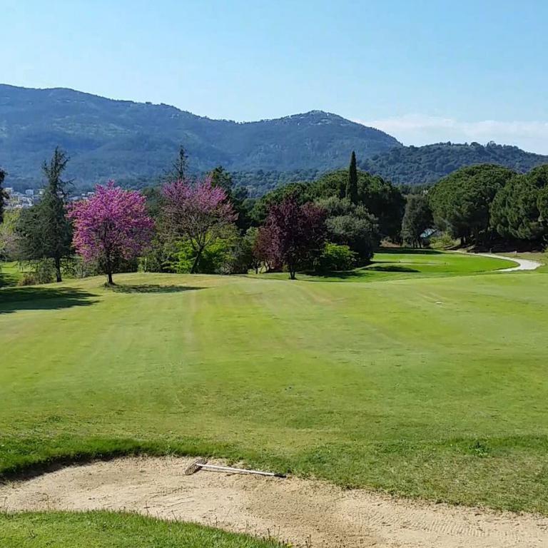 Eine weitläufige Golfanlage mit grüner Wiese, einer Sandbunker und Blick auf bewaldete Hügel und Berge.