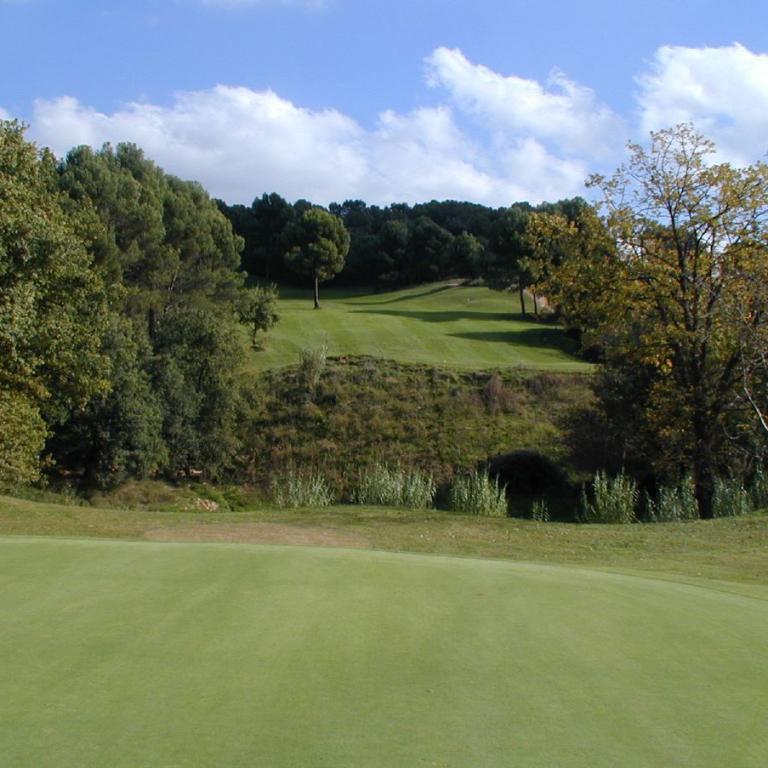 Eine grüne Golfwiese mit einem Blick auf eine baumbestandene Landschaft unter blauem Himmel.