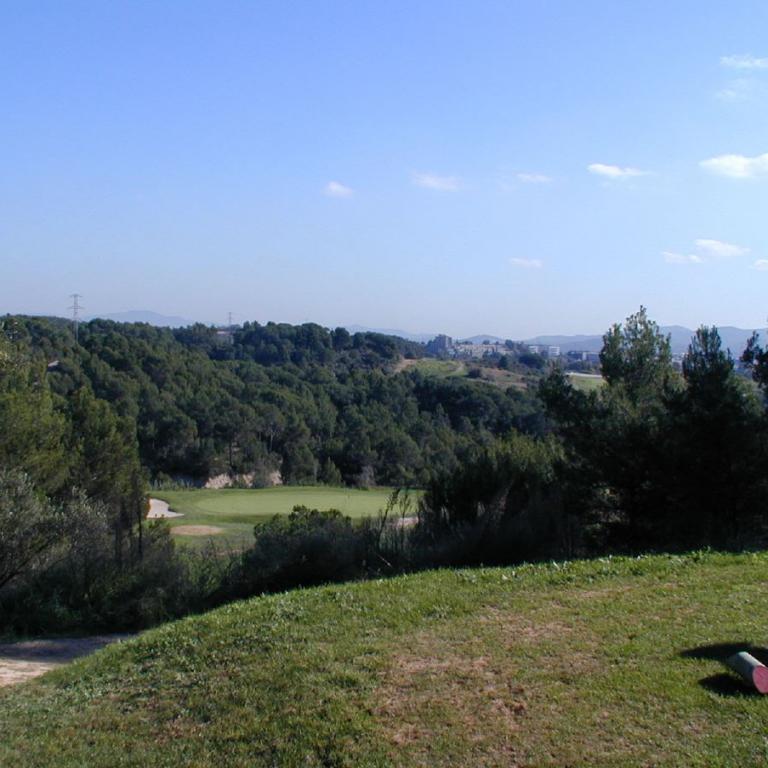 Eine weite Landschaftsaufnahme eines Golfplatzes vor einem Hintergrund aus dicht bewaldeten Hügeln.