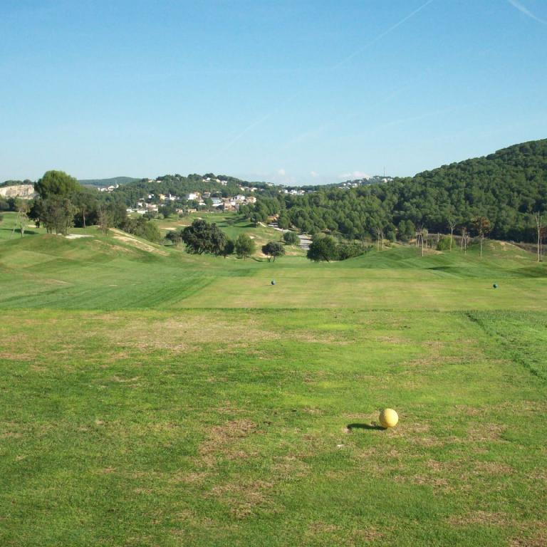 Panoramaaufnahme eines Golfplatzes an einem sonnigen Tag mit Blick auf eine bewaldete Hügellandschaft.