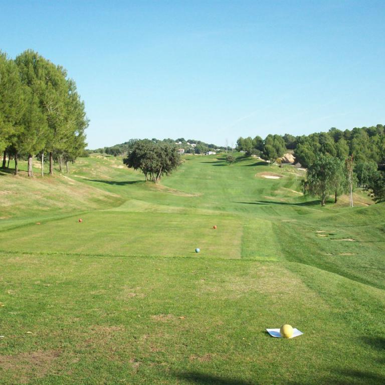 Weitläufiger Blick auf einen gepflegten Golfplatz mit vielen Bäumen und einem klaren blauen Himmel.