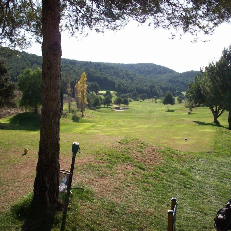 Panoramaansicht eines Golfplatzes mit Blick auf eine hügelige, bewaldete Landschaft.