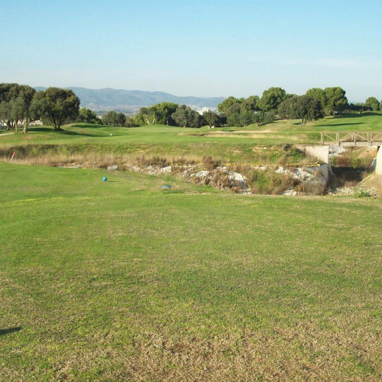 Ein weitläufiger Golfplatz mit gepflegten grünen Gräsfeldern und Blick auf eine bewaldete Hügellandschaft.