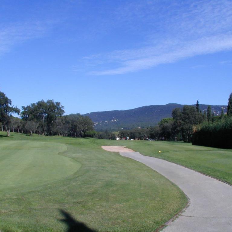 Ein weitläufiger Golfplatz mit einem geschwungenen Weg, umgeben von saftigem Grün und einer bergigen Landschaft unter blauem Himmel.