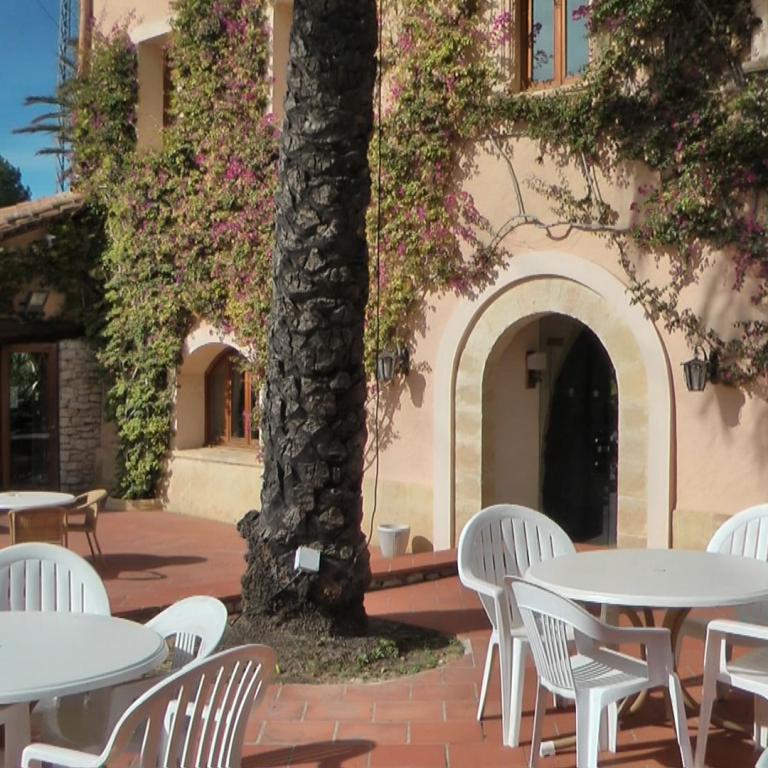 Ein mediterraner Patio mit weißem Outdoor-Mobiliar, umgeben von Gebäuden, die mit pinken, blühenden Kletterpflanzen bewachsen sind.