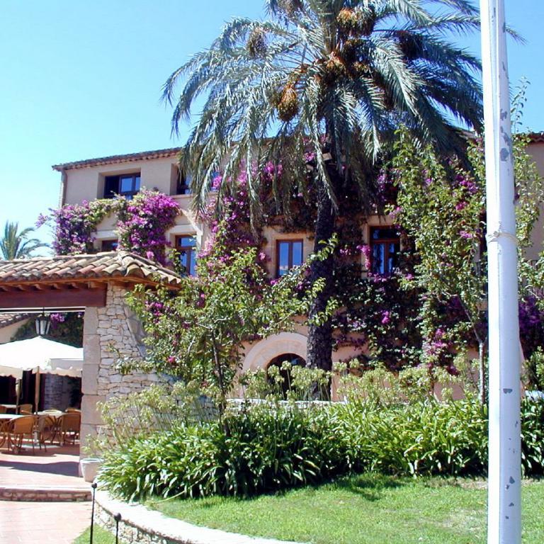 Ein großes, mediterranes Anwesen mit Palmen und blühenden Pflanzen unter blauem Himmel.
