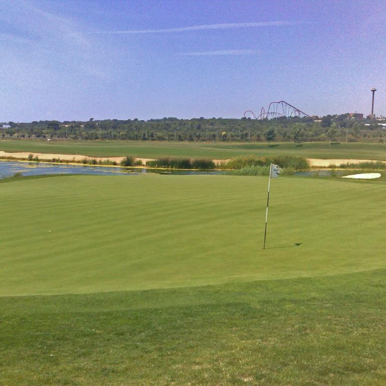 Ein weitläufiges Golfgreen mit einem Fahnenmast und Blick auf einen See und eine dahinterliegende Stadtlandschaft