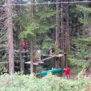 Ein Kletterparcours und Baumhaus-Struktur inmitten eines Waldgebietes mit Menschen, die Aktivitäten ausüben.
