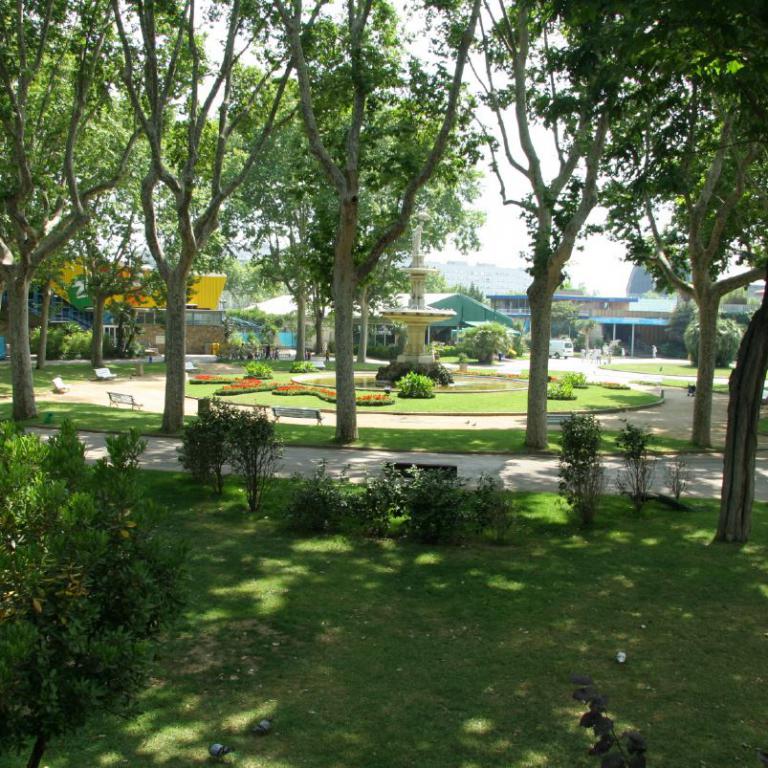 Ein weitläufiger, grüner Stadtpark mit hohen Bäumen, Rasenflächen und gepflegten Wegen.