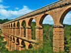 Überreste einer alten Steinbrücke mit mehreren Bögen, die in eine grüne Landschaft führen.