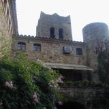 Ansicht eines historischen Gebäudekomplexes aus Stein, der einen zylindrischen Turm und üppige Blumenbegehungen zeigt.