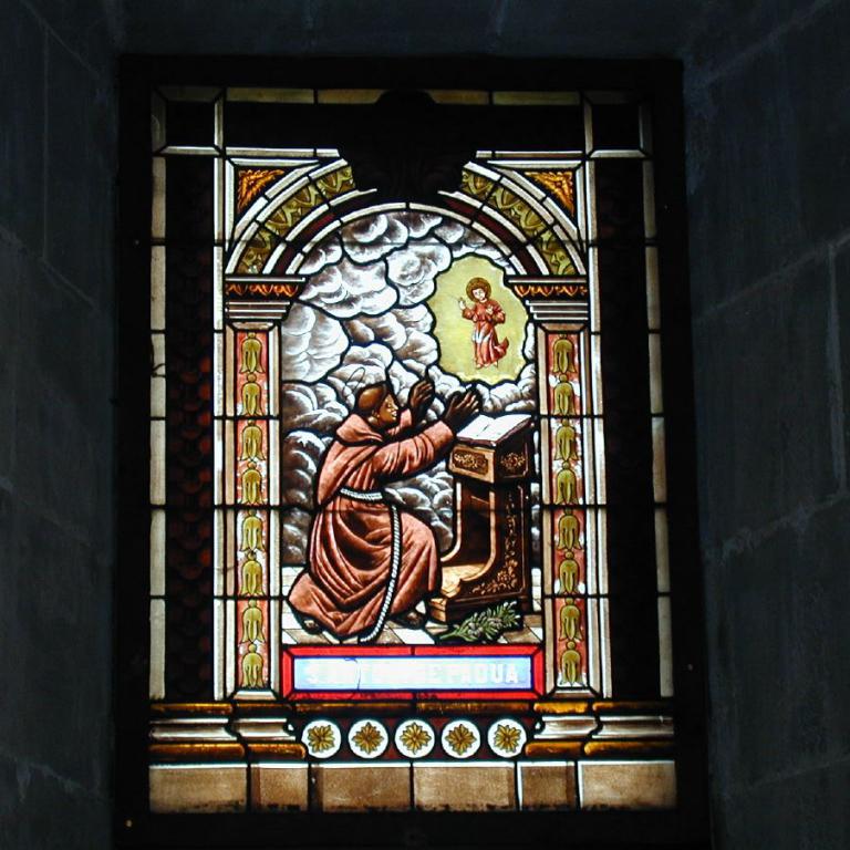 Ein großes Buntglasfenster, das eine religiöse Szene mit einer knienden männlichen Figur vor einem Altar in einem Kircheninneren darstellt.