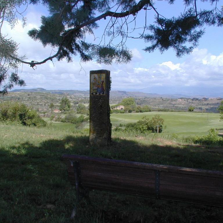 Eine Holzbank im Vordergrund mit Blick auf eine weitläufige, hügelige Landschaft unter einem bewölkten Himmel.