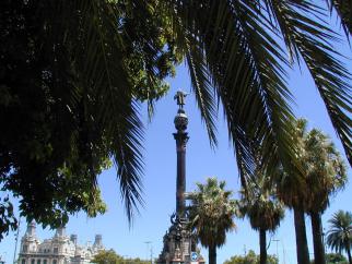 Palmenblätter rahmen einen monumentalen Brunnen und historische Architektur unter einem strahlend blauen Himmel ein.