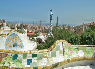 Ein Panorama aus einer Parkanlage, das durch einen farbenprächtigen Mosaikbogen und einen markanten Turm im Mittelgrund dominiert wird, mit Blick auf