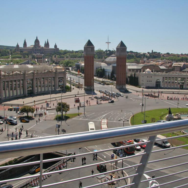 Panoramaansicht eines weiten, belebten historischen Stadtplatzes mit markanten Gebäuden und Türmen unter blauem Himmel.