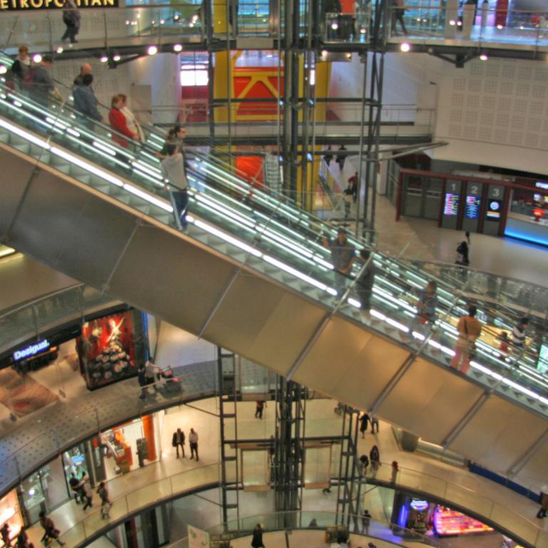 Ein weitläufiger Blick auf das Innere einer modernen, mehrstöckigen Bahnhofshalle mit vielen Rolltreppen und Passanten.