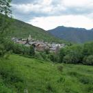 Ein Dorf in einem tiefgrünen Tal, umgeben von steilen, bewaldeten Berghängen.